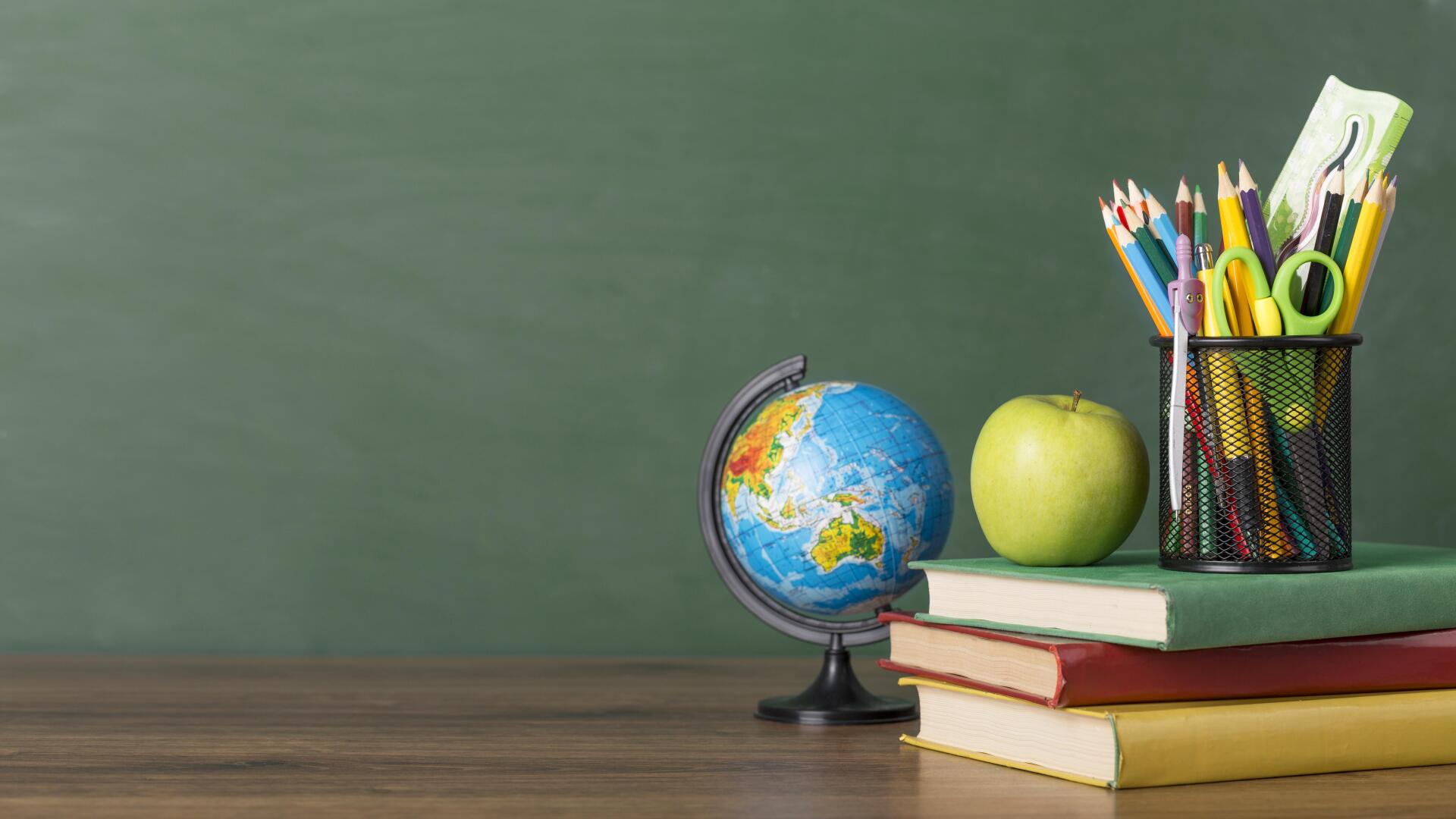 A stack of books , a globe , an apple and pencils on a wooden table.