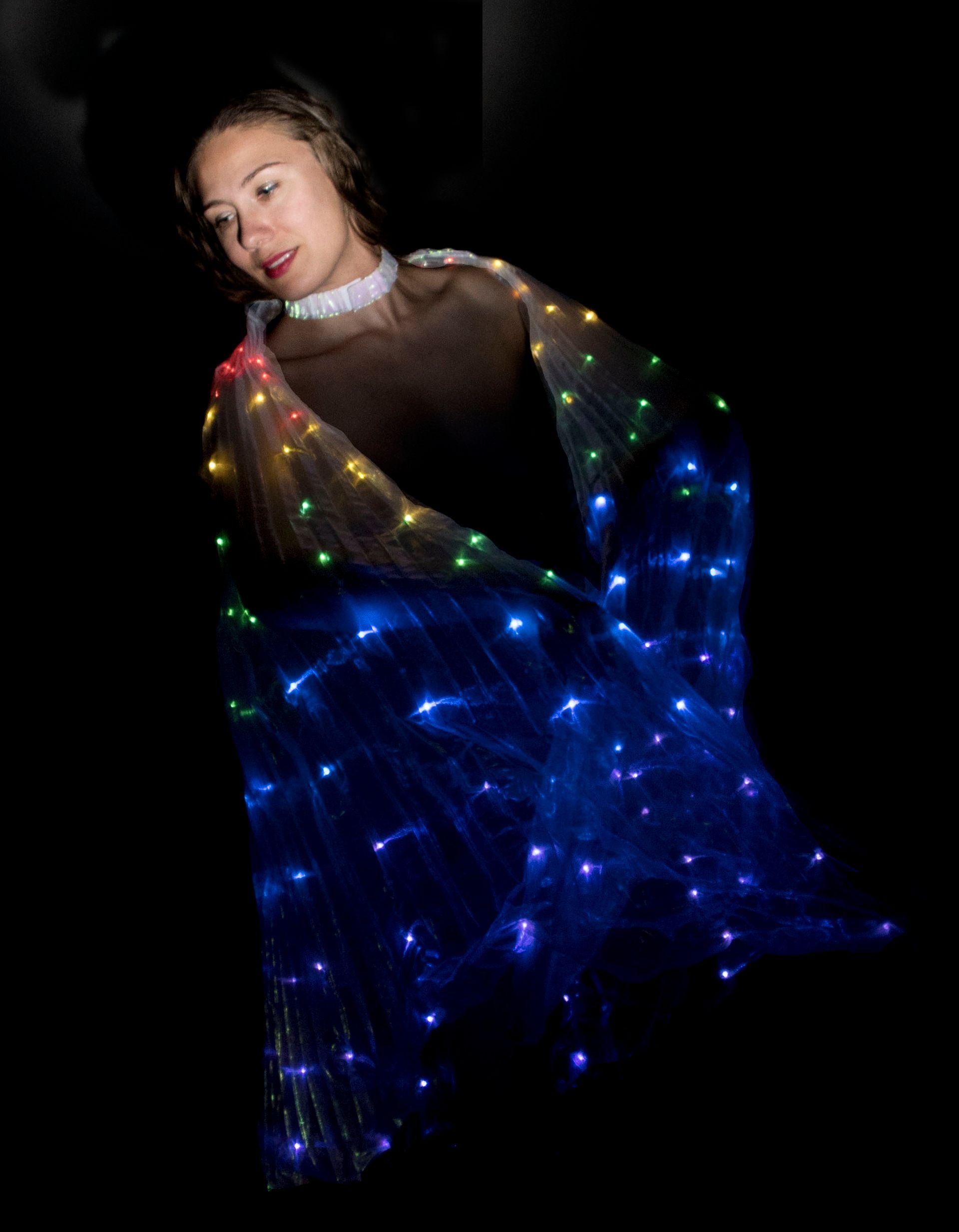 Persoon op een donkere achtergrond, gehuld in blauwe, groene en rode fonkelende lichtjes, kijkt over zijn schouder.
