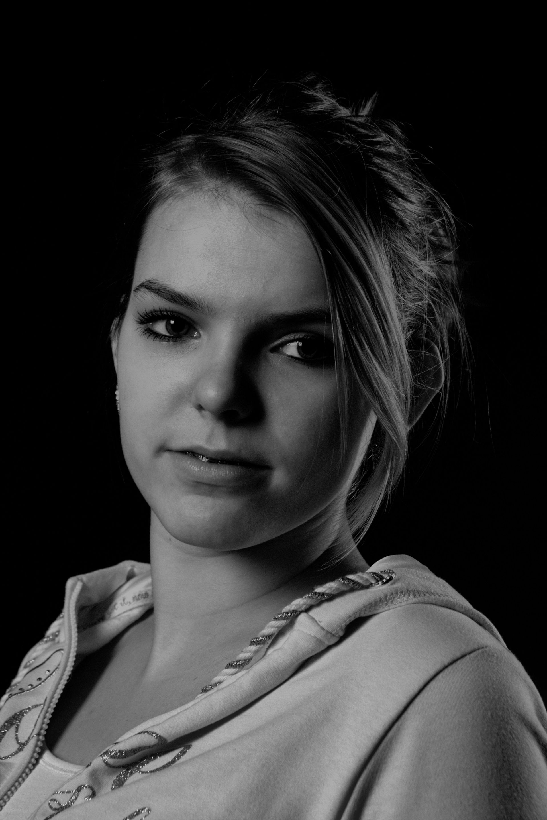 Zwart-wit portret van een persoon in een hoodie, die met een neutrale uitdrukking in de camera kijkt.