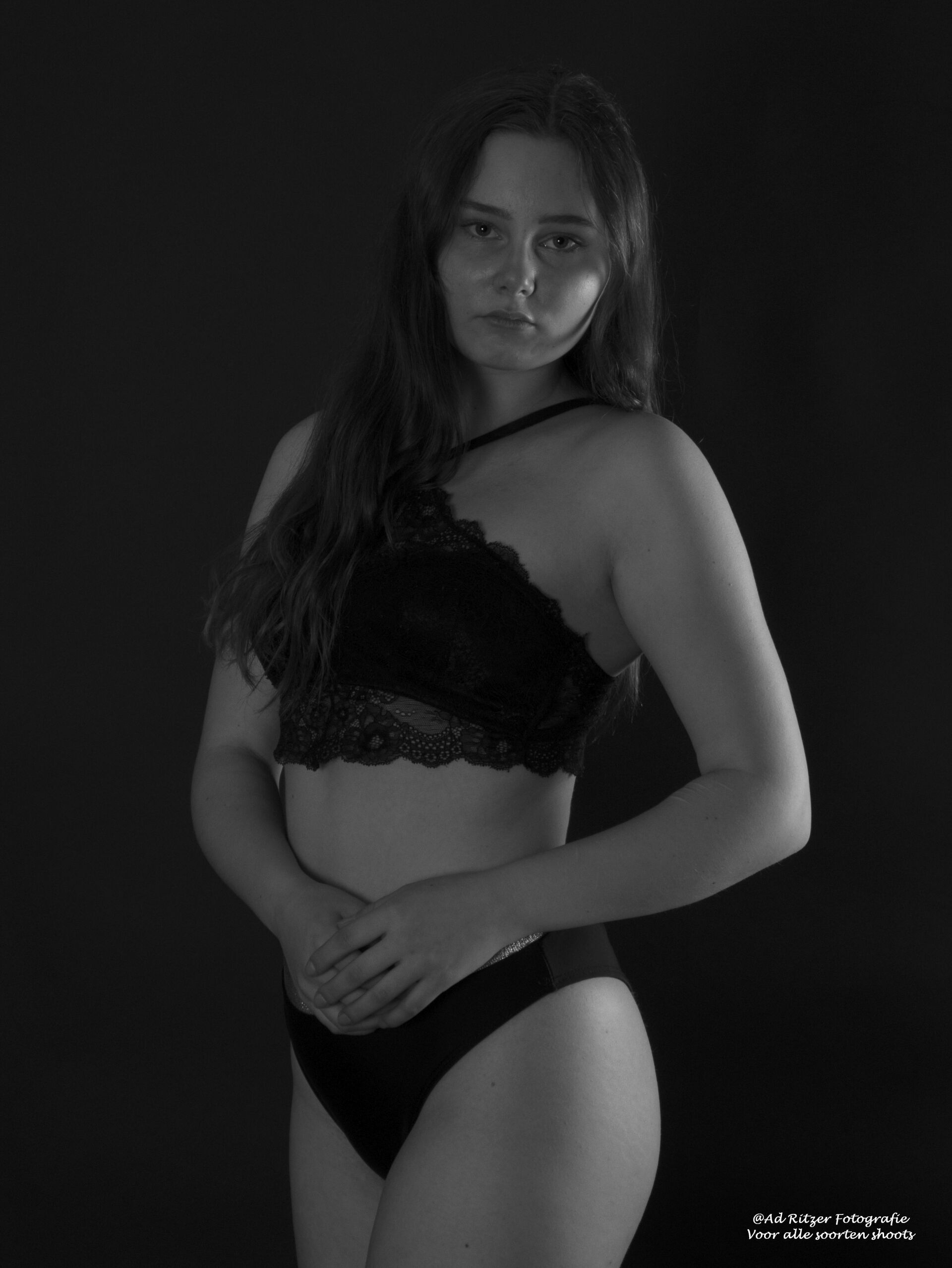 Vrouw poseert in zwarte kanten lingerie tegen een donkere achtergrond.