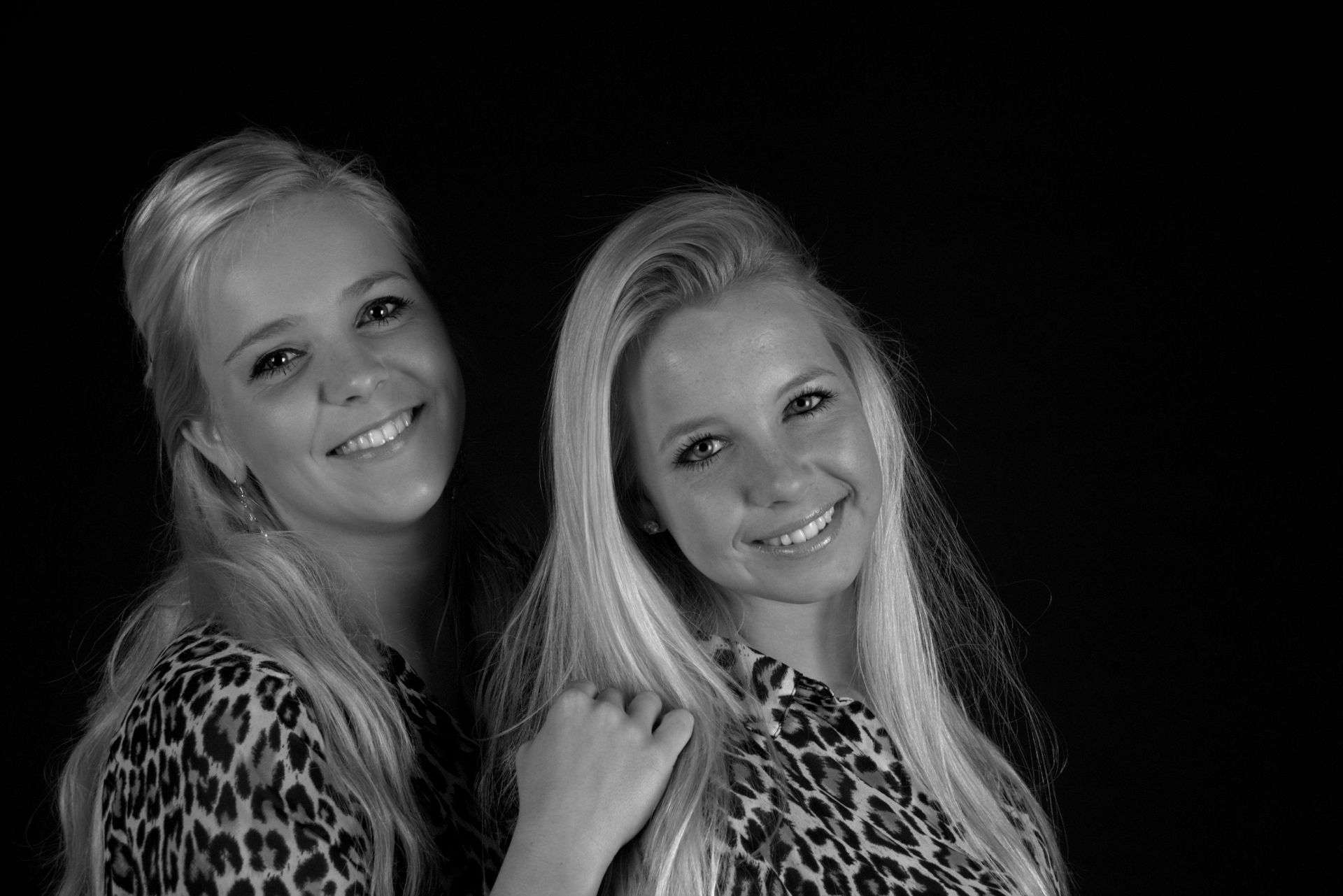 Twee lachende vrouwen in topjes met luipaardprint poseren tegen een zwarte achtergrond.