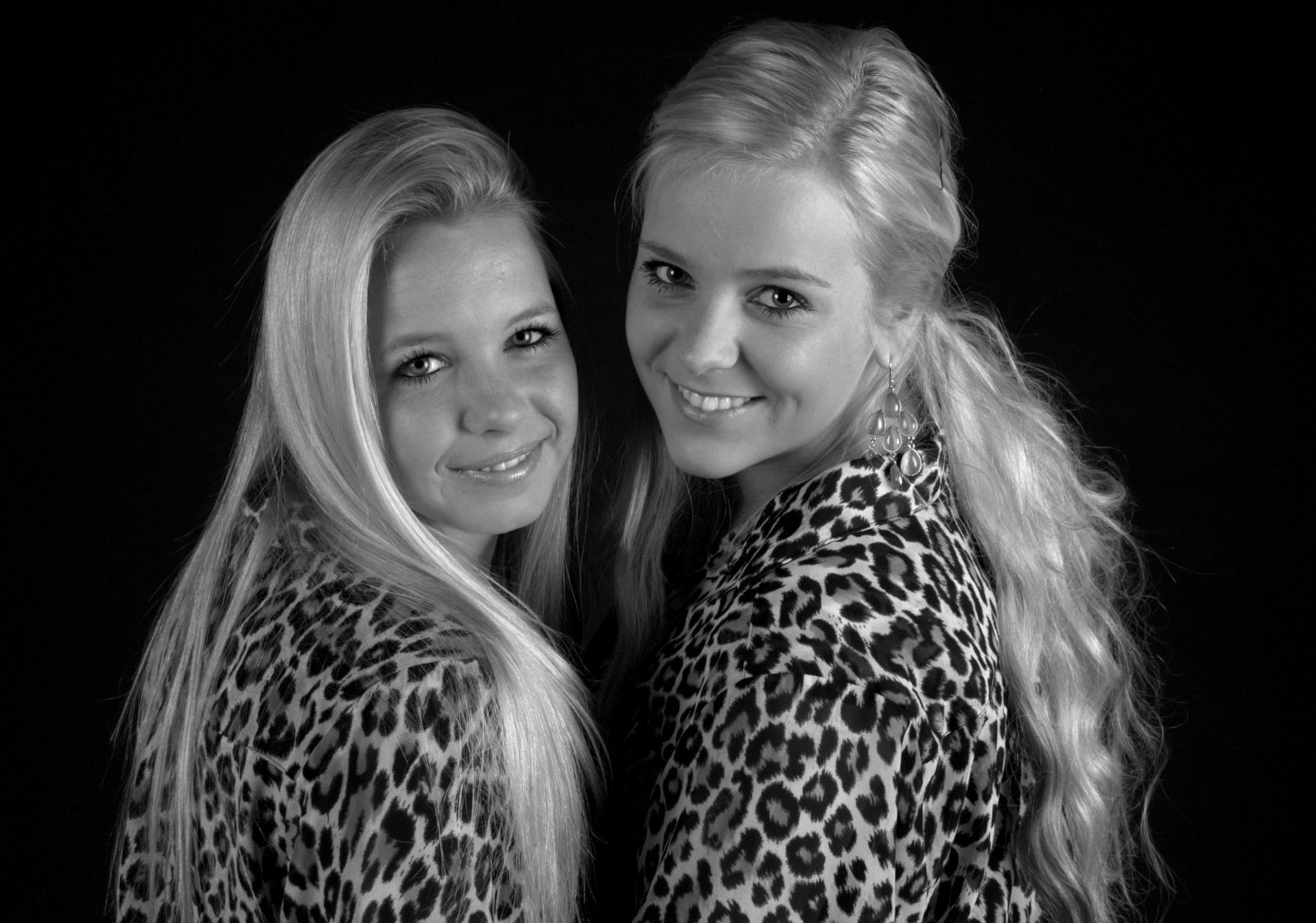 Twee lachende vrouwen in topjes met luipaardprint poseren tegen een zwarte achtergrond.