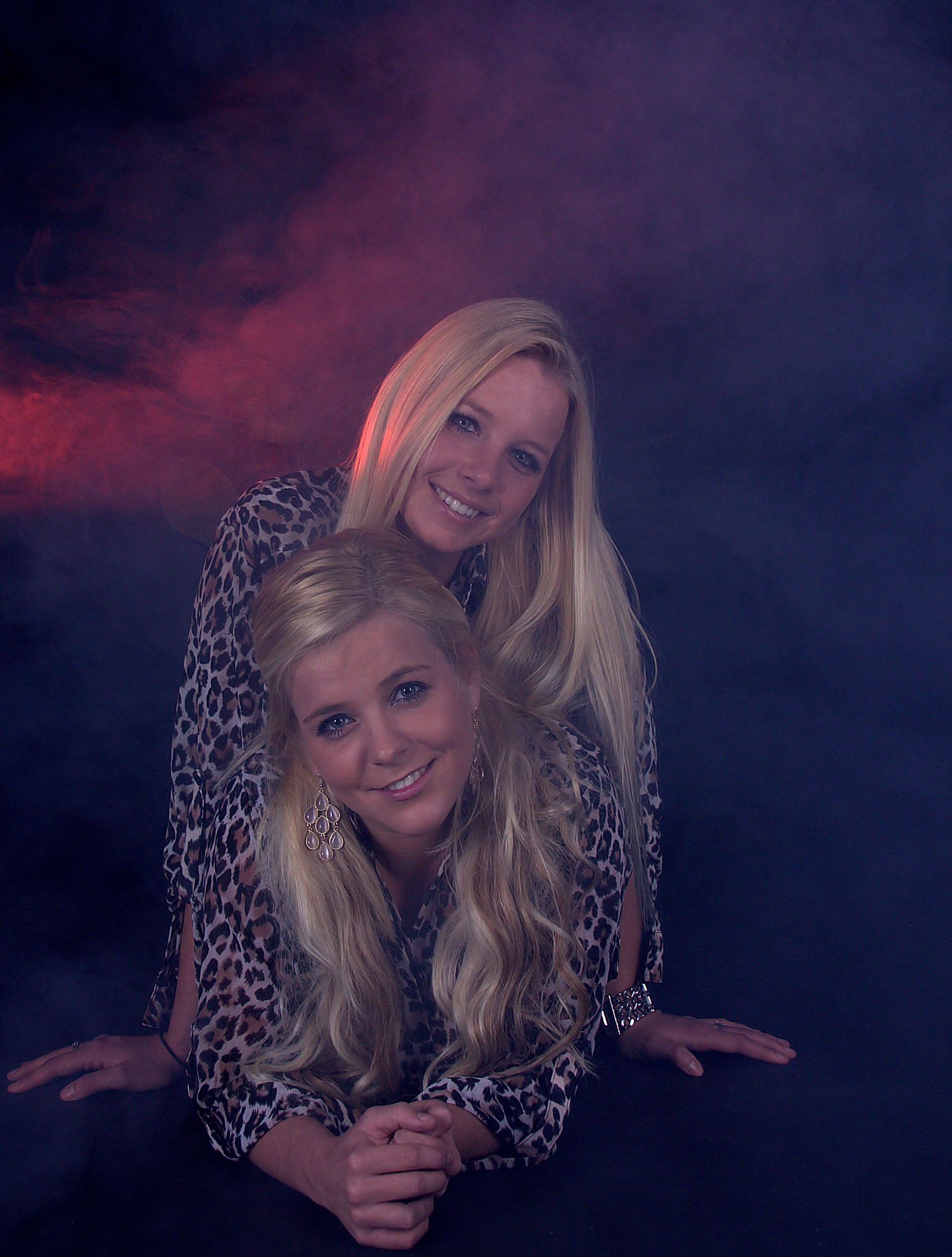 Twee lachende vrouwen poseren samen voor een donkerpaarse en rode studioachtergrond.