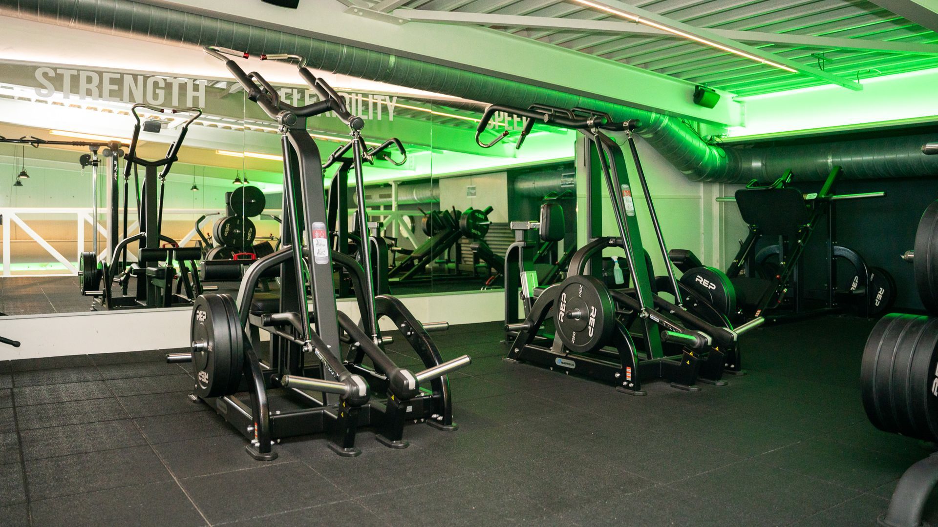 Een sportschool met veel fitnessapparatuur en groene verlichting.