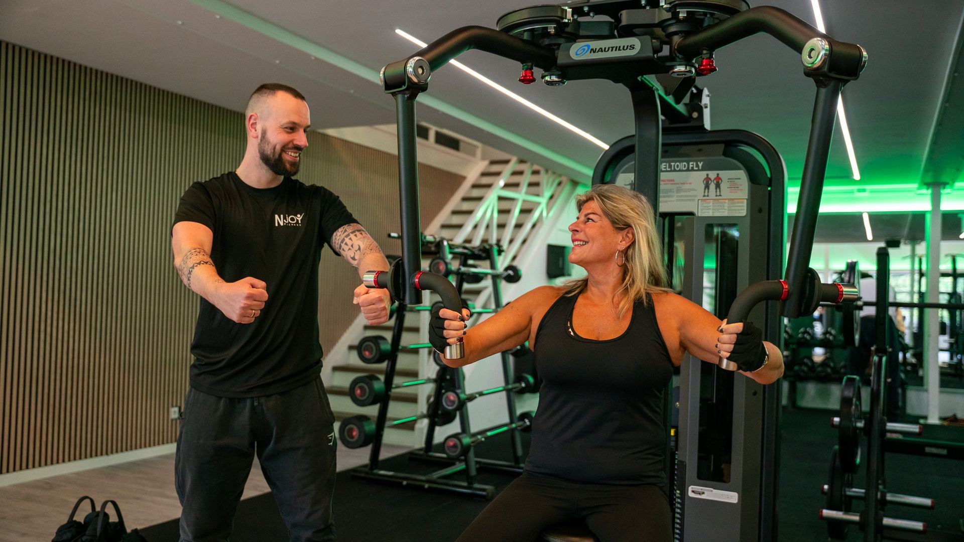Een man helpt een vrouw met het gebruiken van een apparaat in een sportschool.
