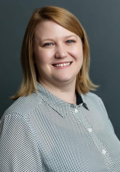Smiling person in a light patterned blouse against a dark gray background