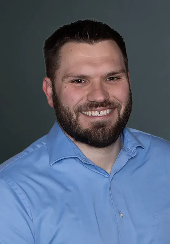 Smiling man in a light blue shirt against a gray studio background