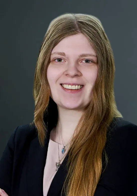 Studio portrait of a smiling person with long light brown hair in a black blazer on a gray background