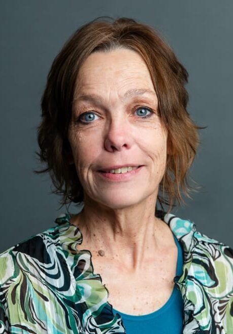 Portrait of a woman with blue eyes, wearing a green patterned top, against a dark background