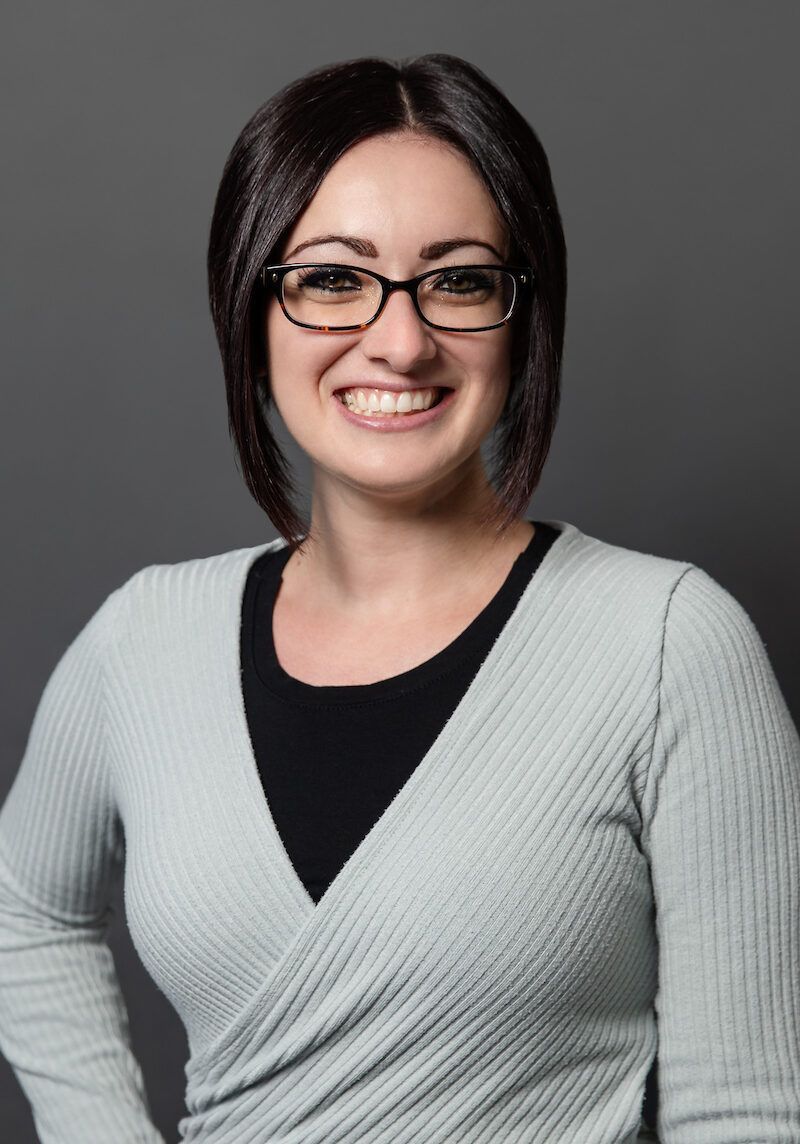 Smiling person with glasses in a gray sweater against a dark background