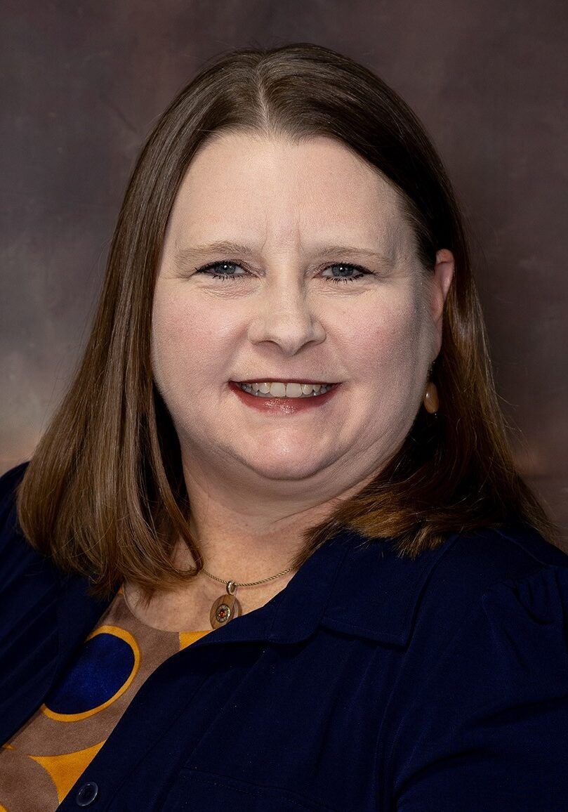Portrait of a smiling person in a navy blazer against a studio backdrop