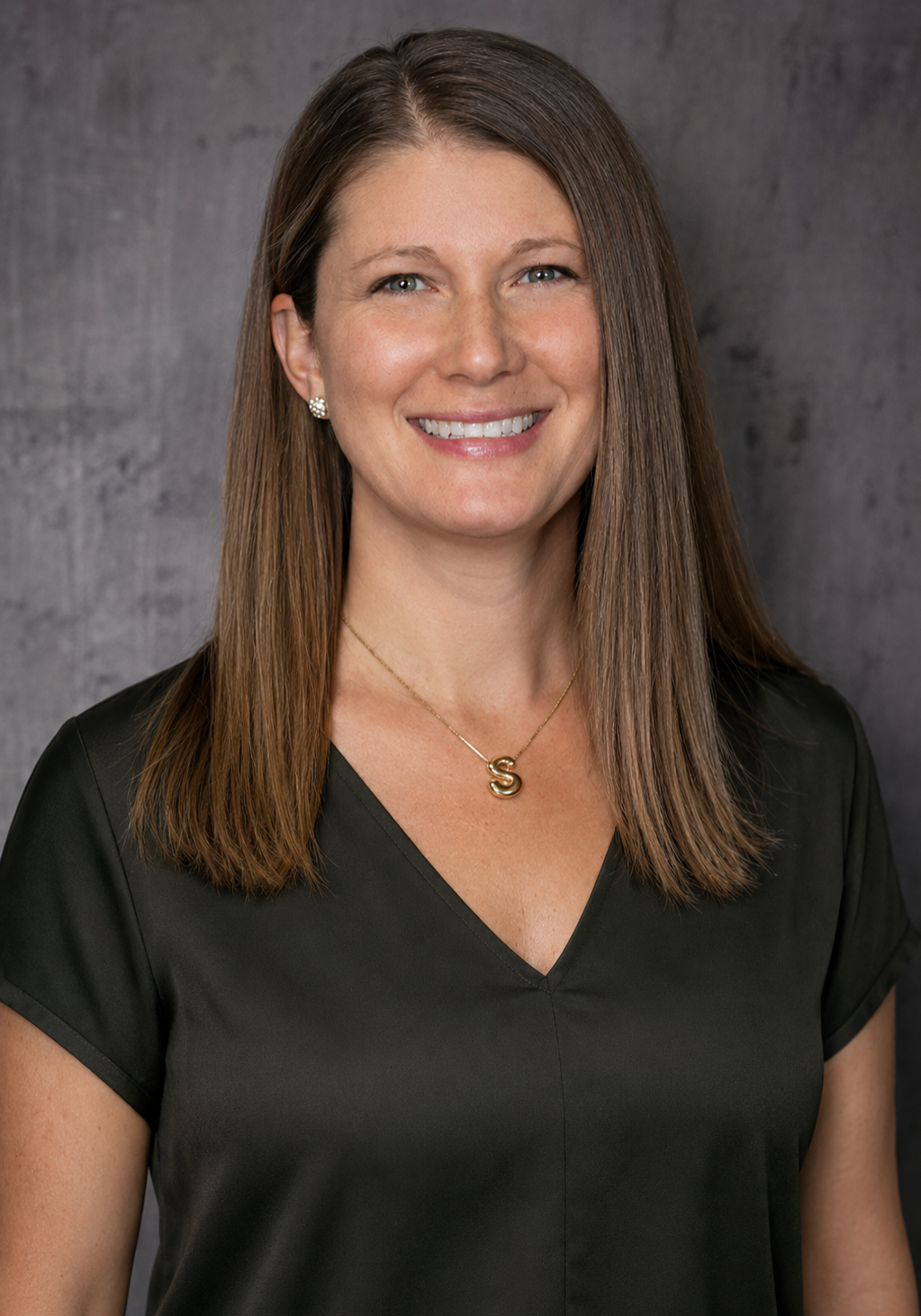 Portrait of a smiling woman in a dark green V-neck top against a gray backdrop