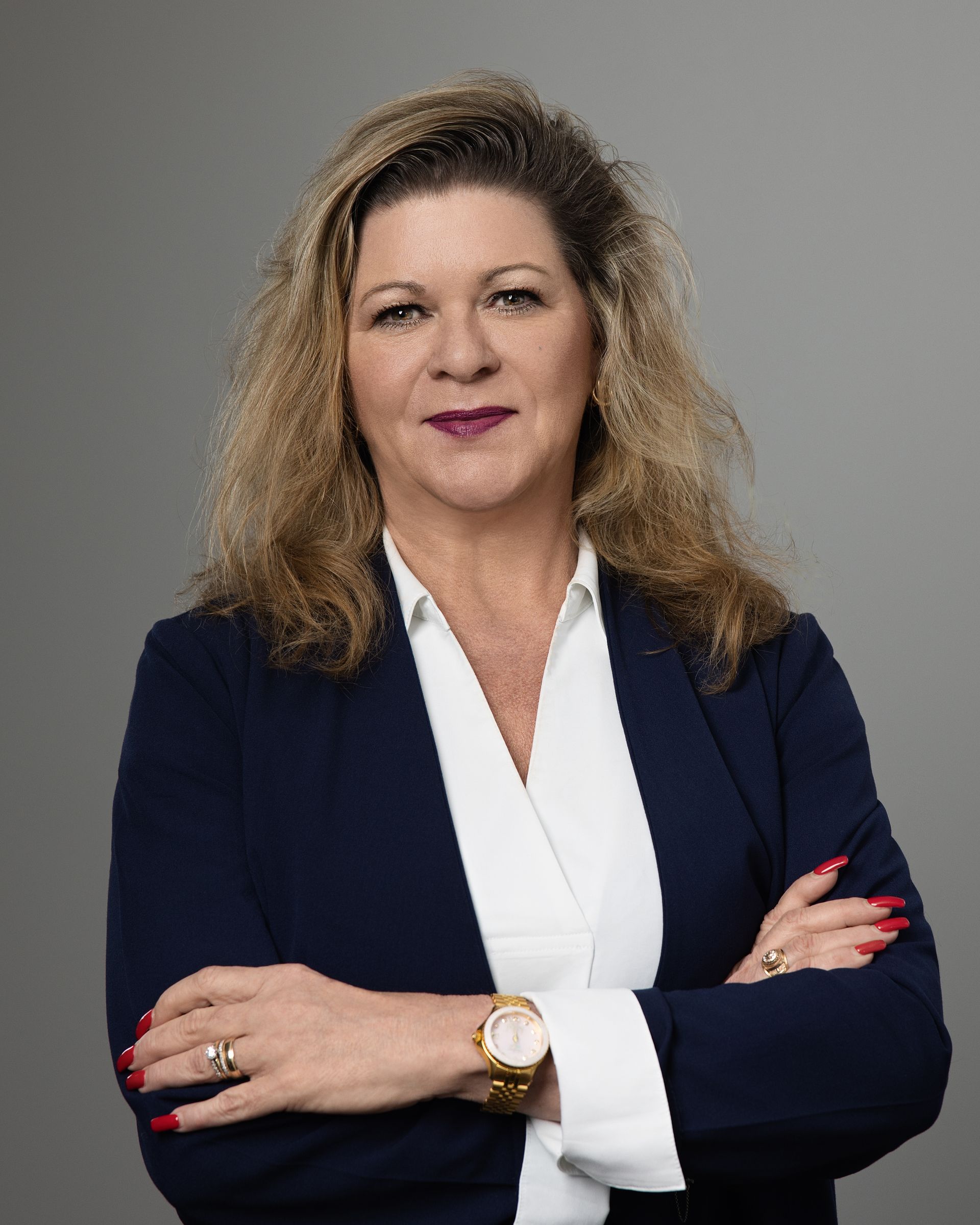 A woman in a blue jacket and white shirt is standing with her arms crossed.