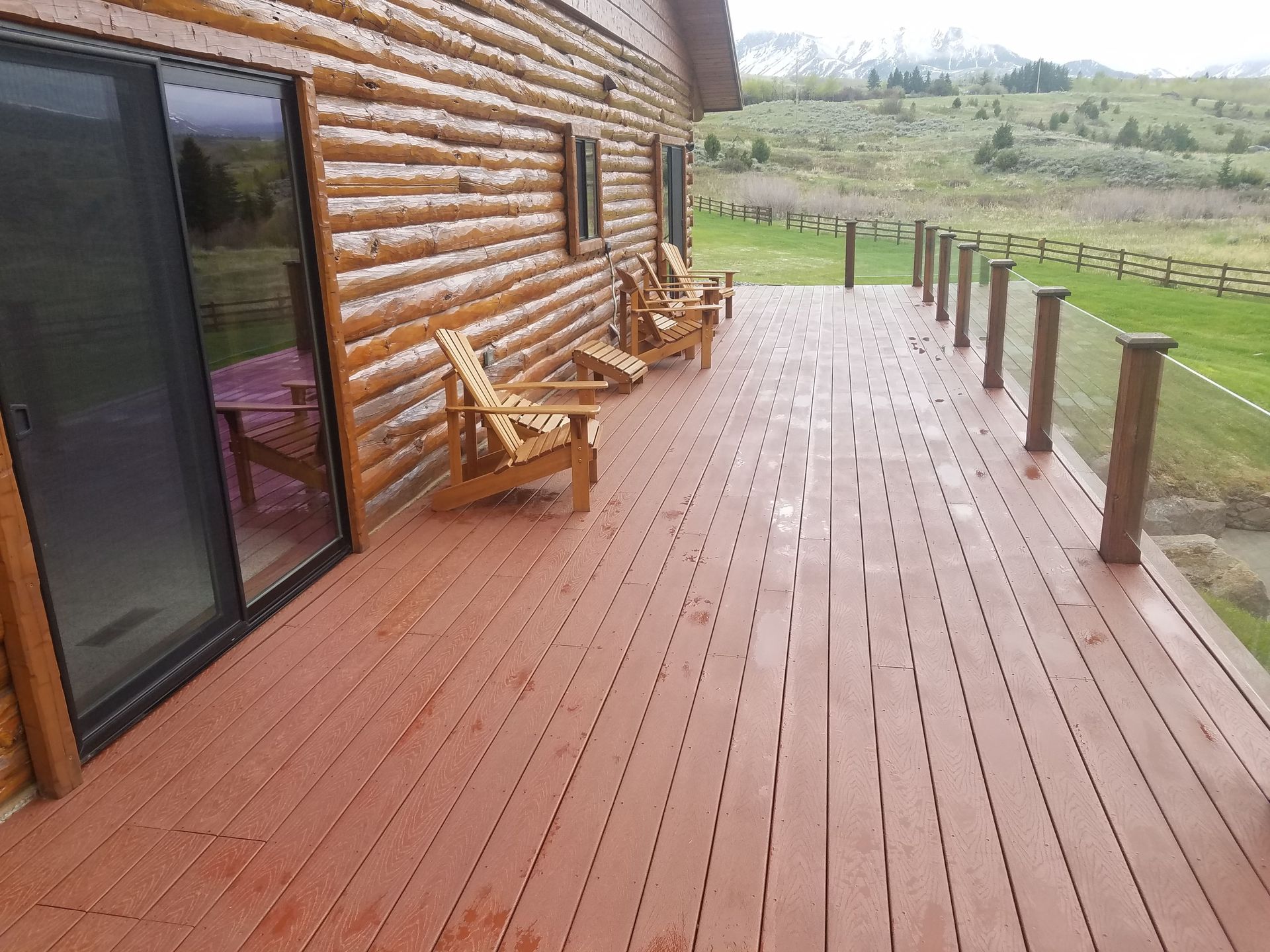 A wooden deck with chairs on it in front of a log cabin.
