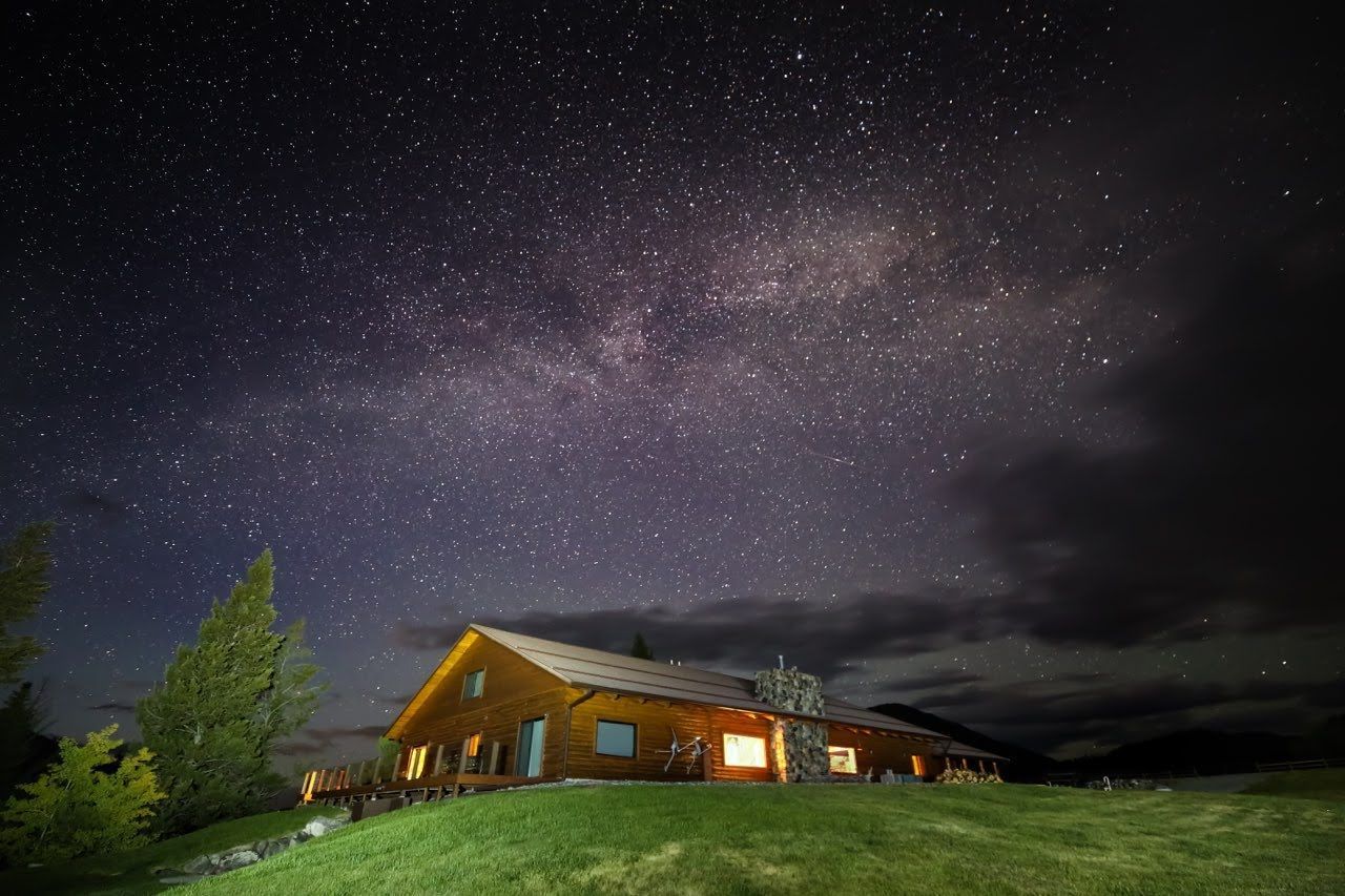 A log cabin is lit up at night under a starry sky.