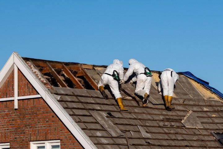 Three workers in white suits repairing a roof under blue sky