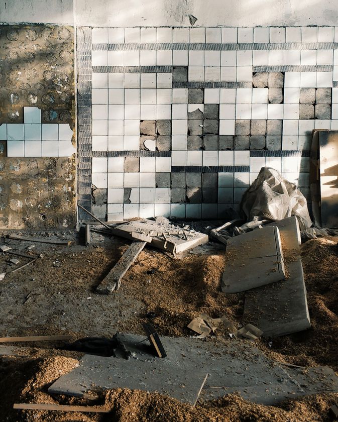 Damaged wall with broken tiles, debris, and rubble in a construction or demolition site.