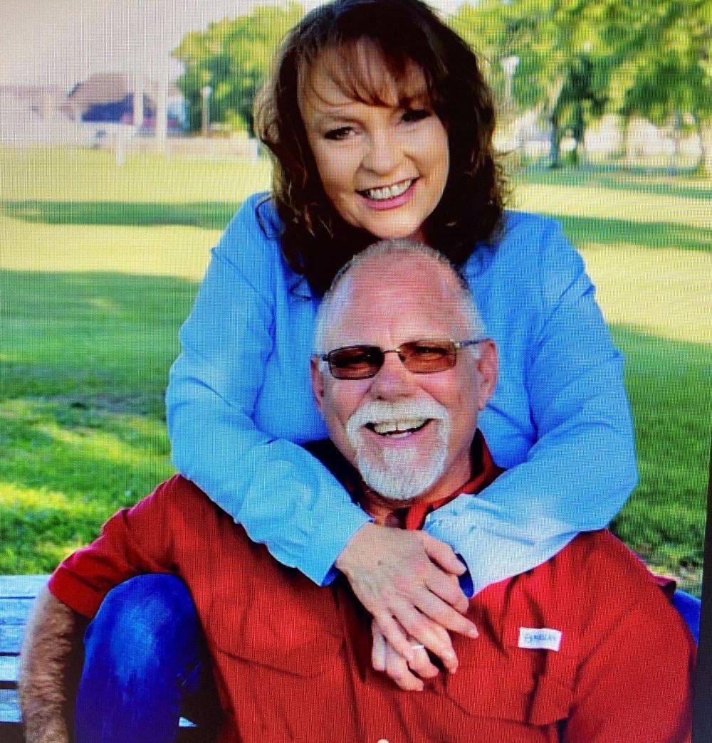 Woman hugs man sitting on bench; both smile in park setting.