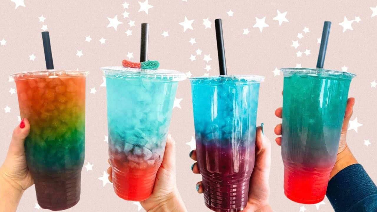 A person is holding four different colored drinks with straws in their hands.