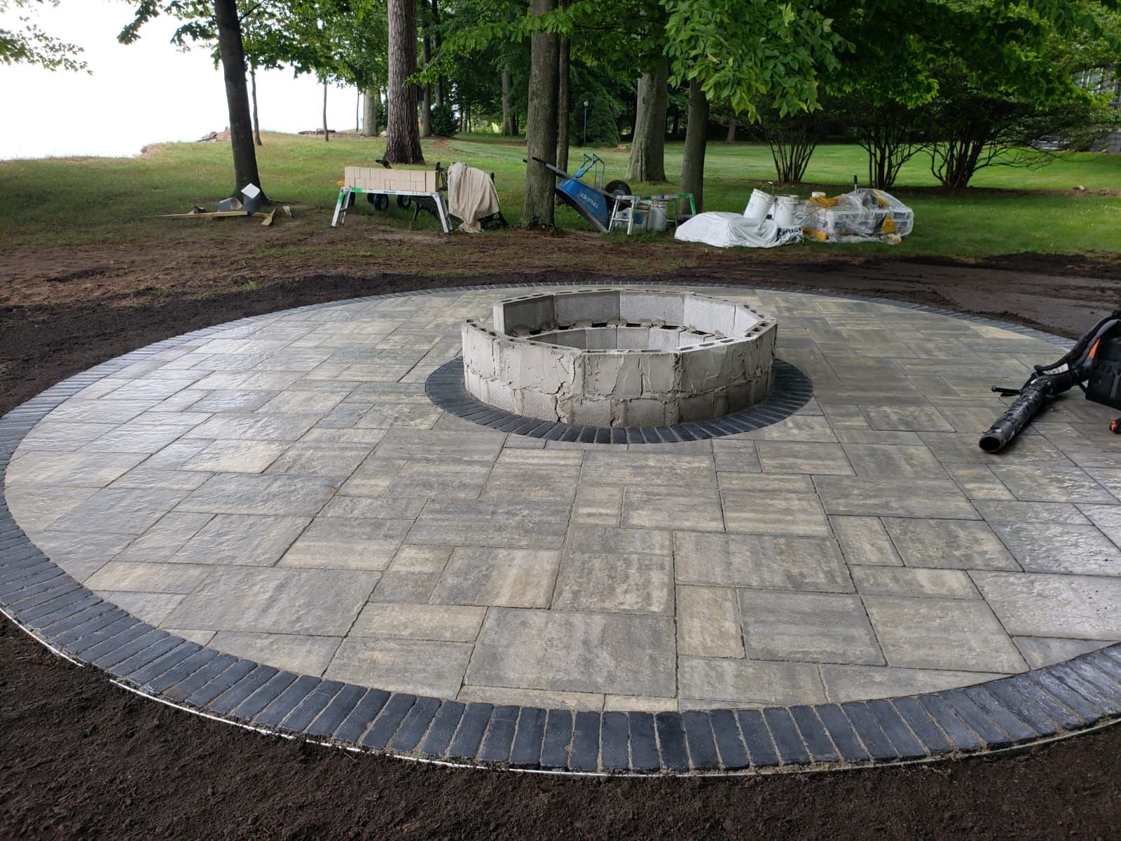 Circular brick patio with fire pit, dark border, and surrounding landscaping.
