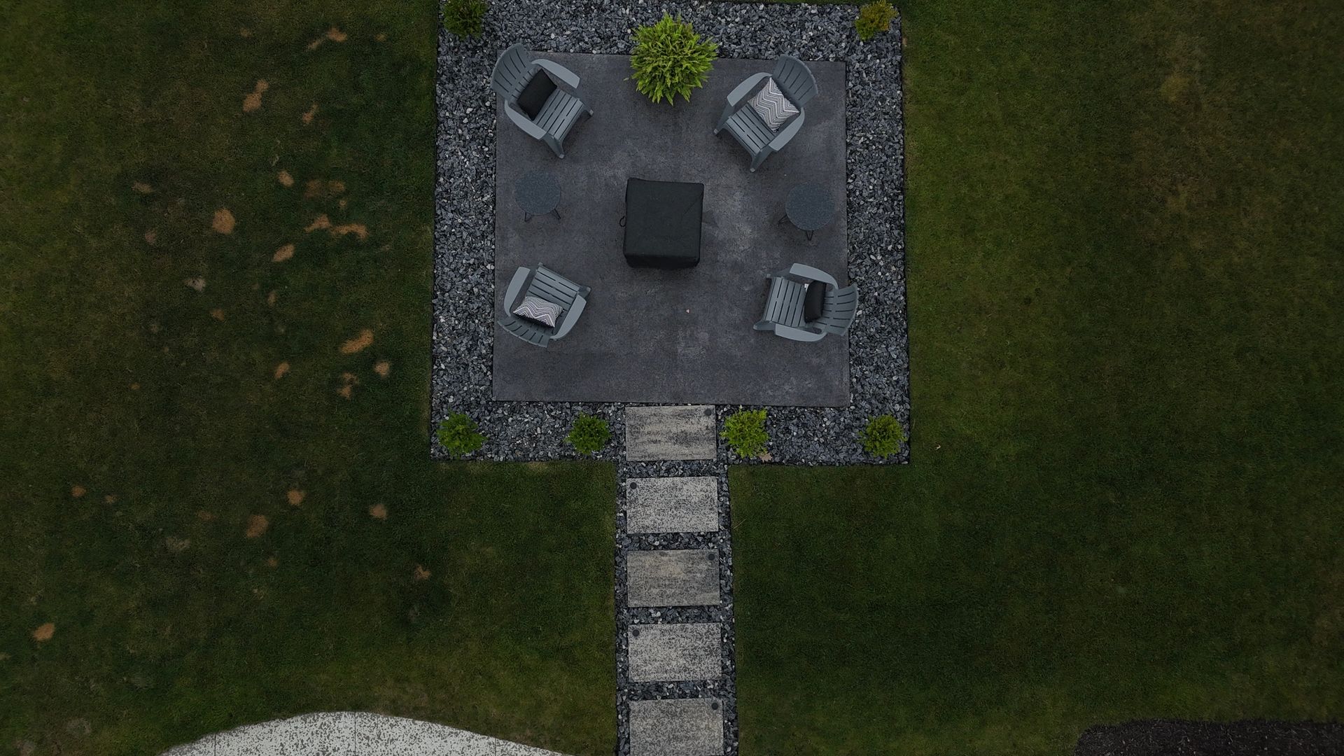 Overhead view of a patio with four chairs around a table, surrounded by dark stones and grass.