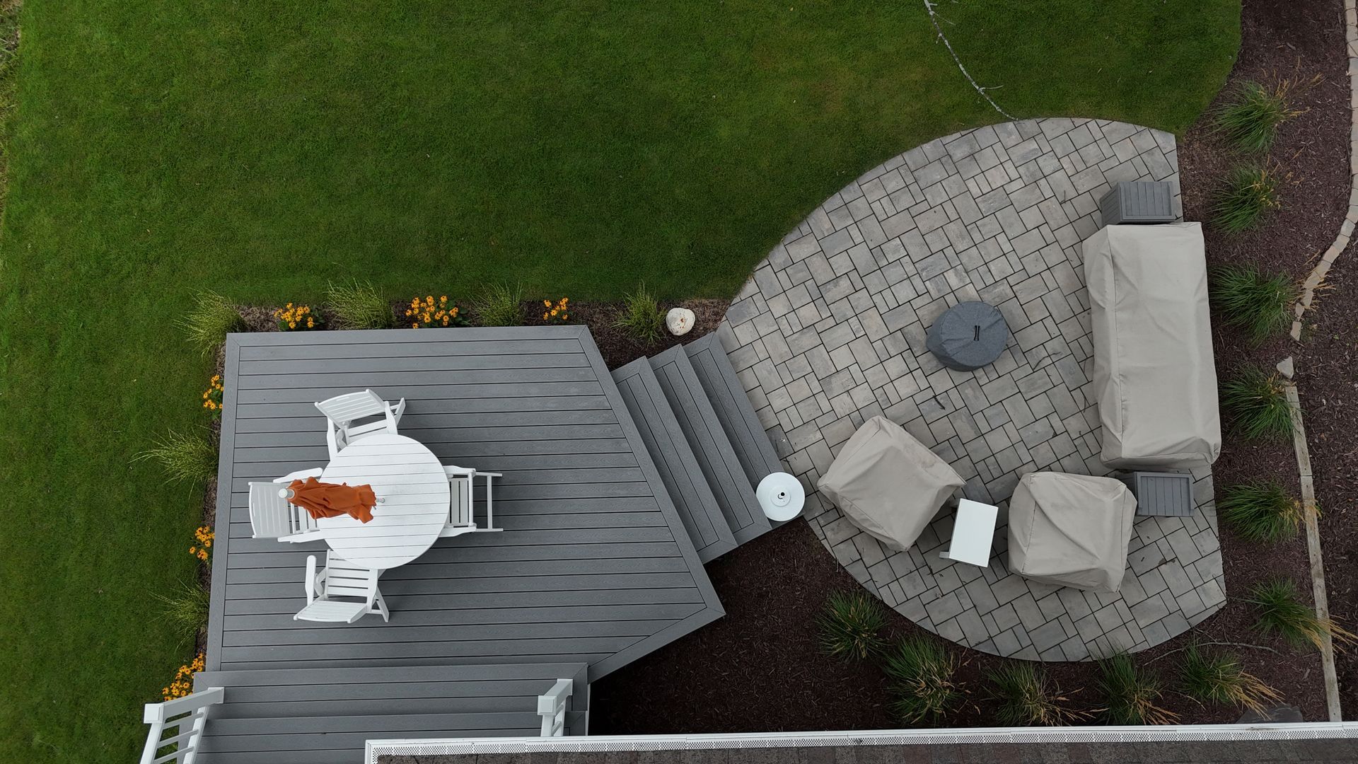Overhead view of a backyard patio with a deck, seating area, and landscaping.