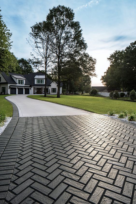 Herringbone brick driveway leading to a white house with a green lawn.