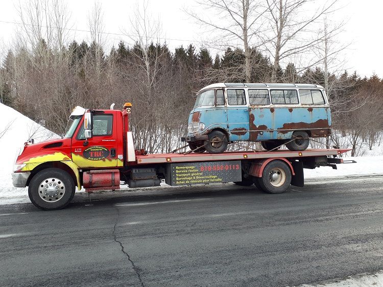 Une dépanneuse transporte un bus bleu rouillé sur le bord d'une route enneigée.