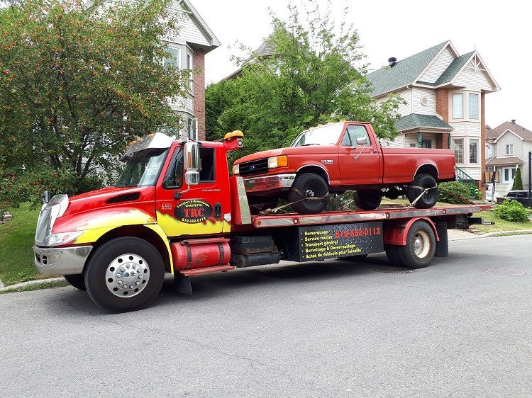 Une dépanneuse rouge, avec une camionnette rouge sur son plateau, est stationnée dans une rue devant des maisons.