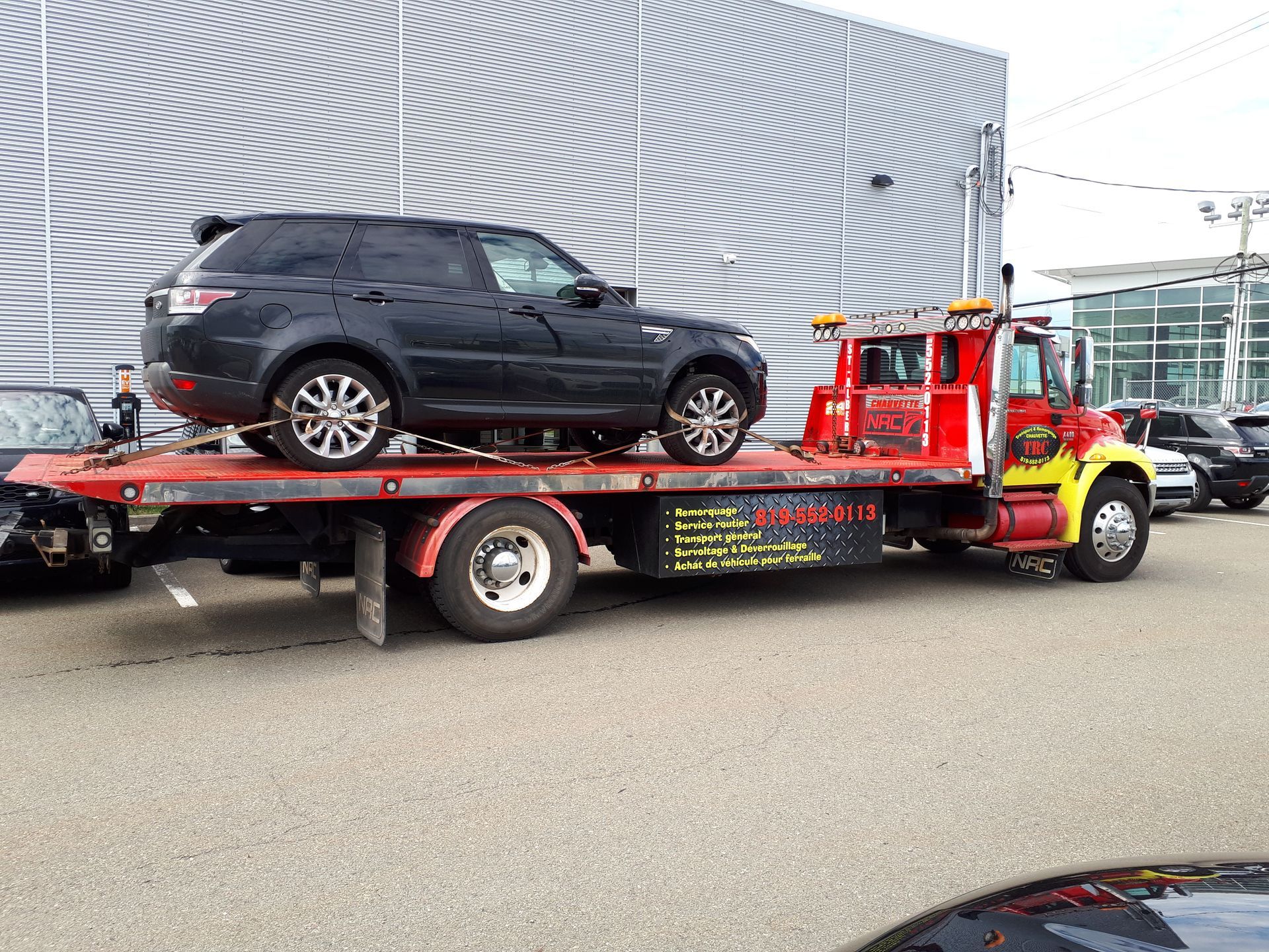 Un SUV noir est remorqué sur une dépanneuse à plateau devant un bâtiment.