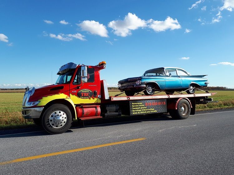 Une dépanneuse rouge et jaune transporte une voiture classique bleu clair par une journée ensoleillée.