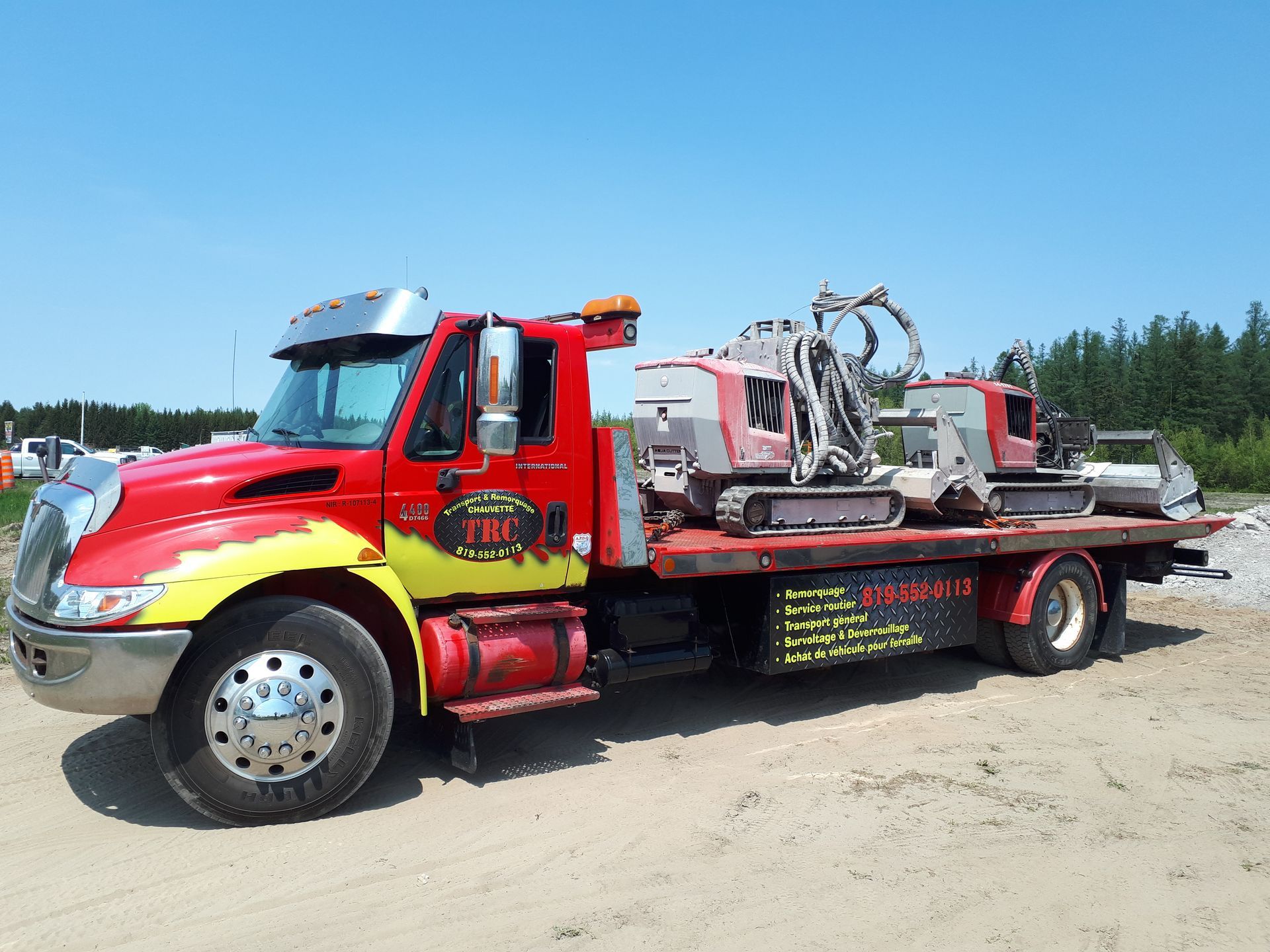 Camion de dépannage rouge transportant du matériel de chantier par une journée ensoleillée.