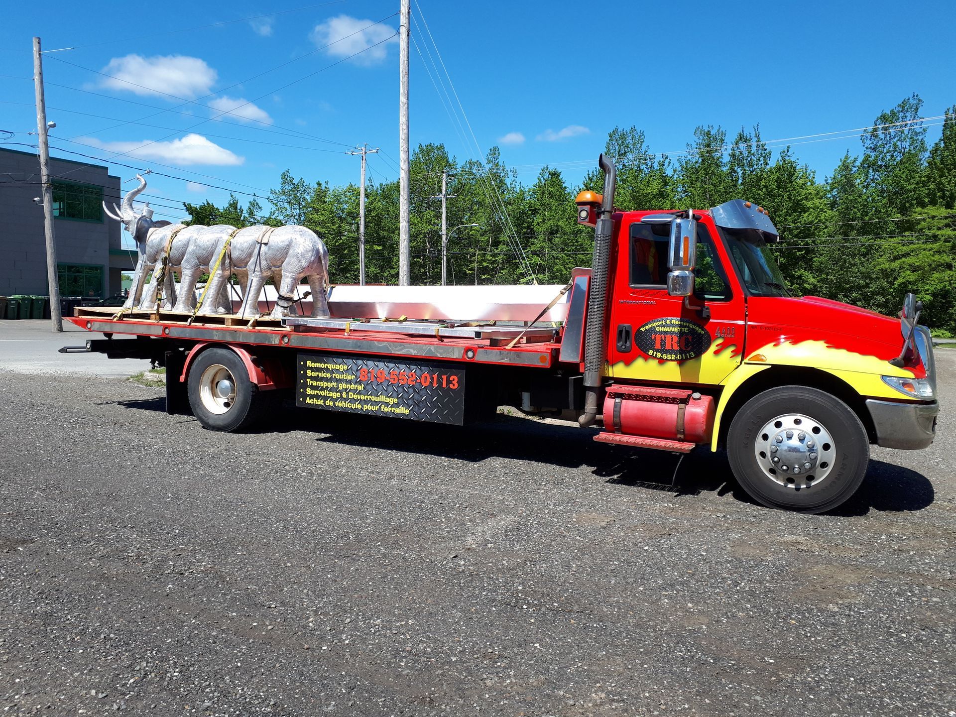 Un camion de dépannage rouge transportant des sculptures d'animaux blanches par une journée ensoleillée.
