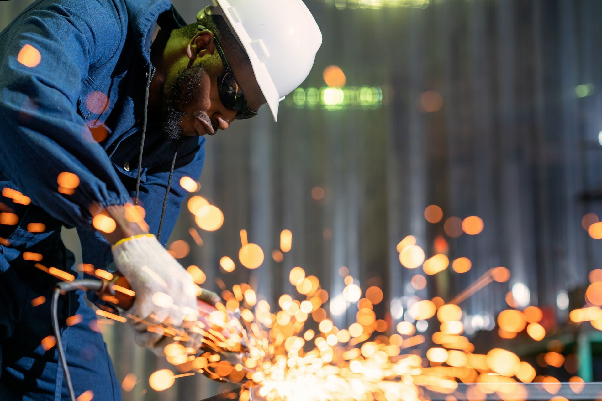 Person in protective gear grinding metal, creating sparks in a factory setting.