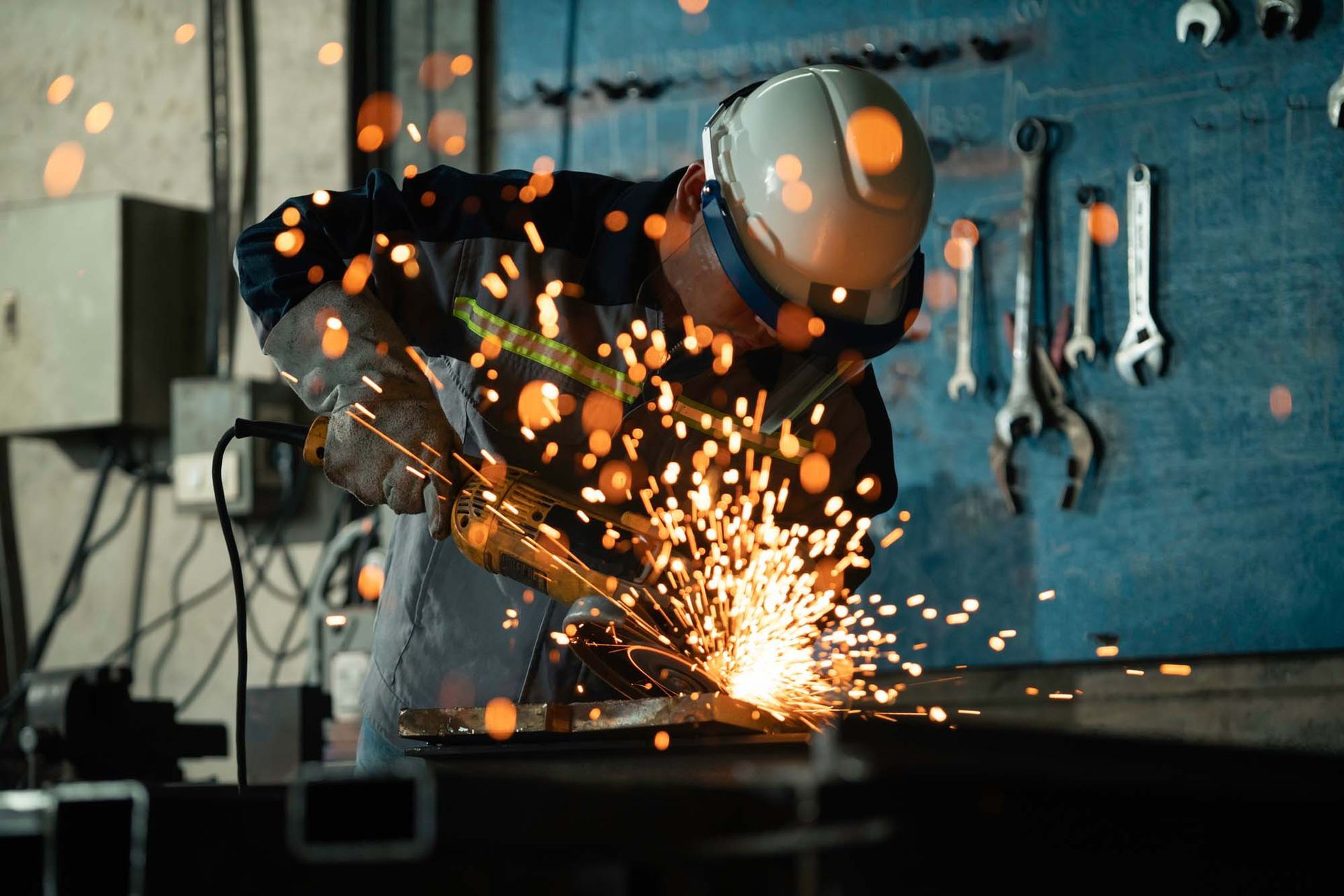 Worker in hard hat grinding metal, sparks flying in a workshop.