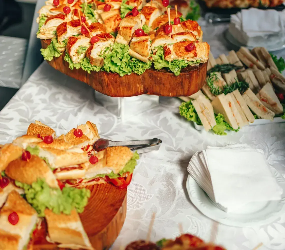 A buffet table featuring platters of sandwiches and bite-sized appetizers, with a hand reaching toward the food.