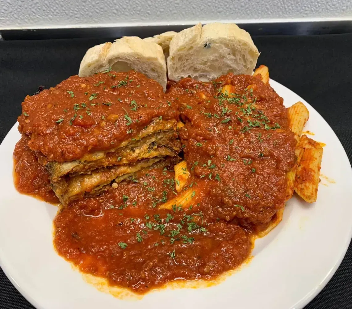 A plate of lasagna topped with red sauce and herbs, served with a side of fries and sliced bread on a black background.