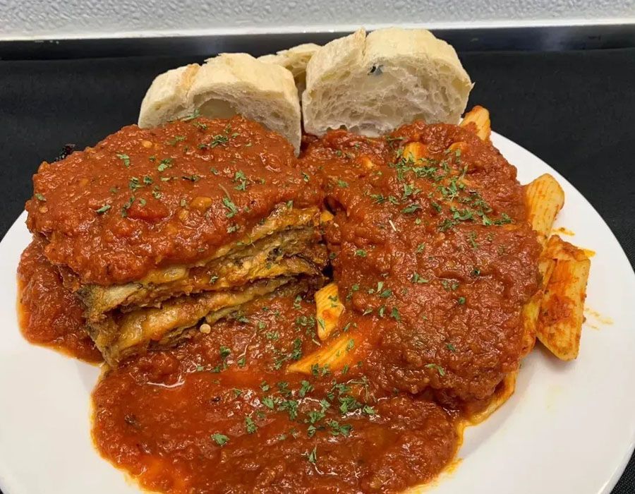 A plate of lasagna topped with red sauce and herbs, served with a side of fries and sliced bread on a black background.