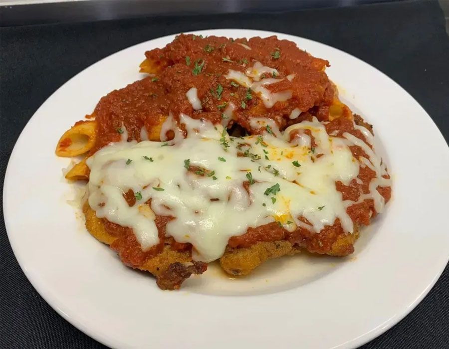 A breaded chicken parmigiana topped with melted mozzarella, marinara sauce, and herbs, served with penne pasta.