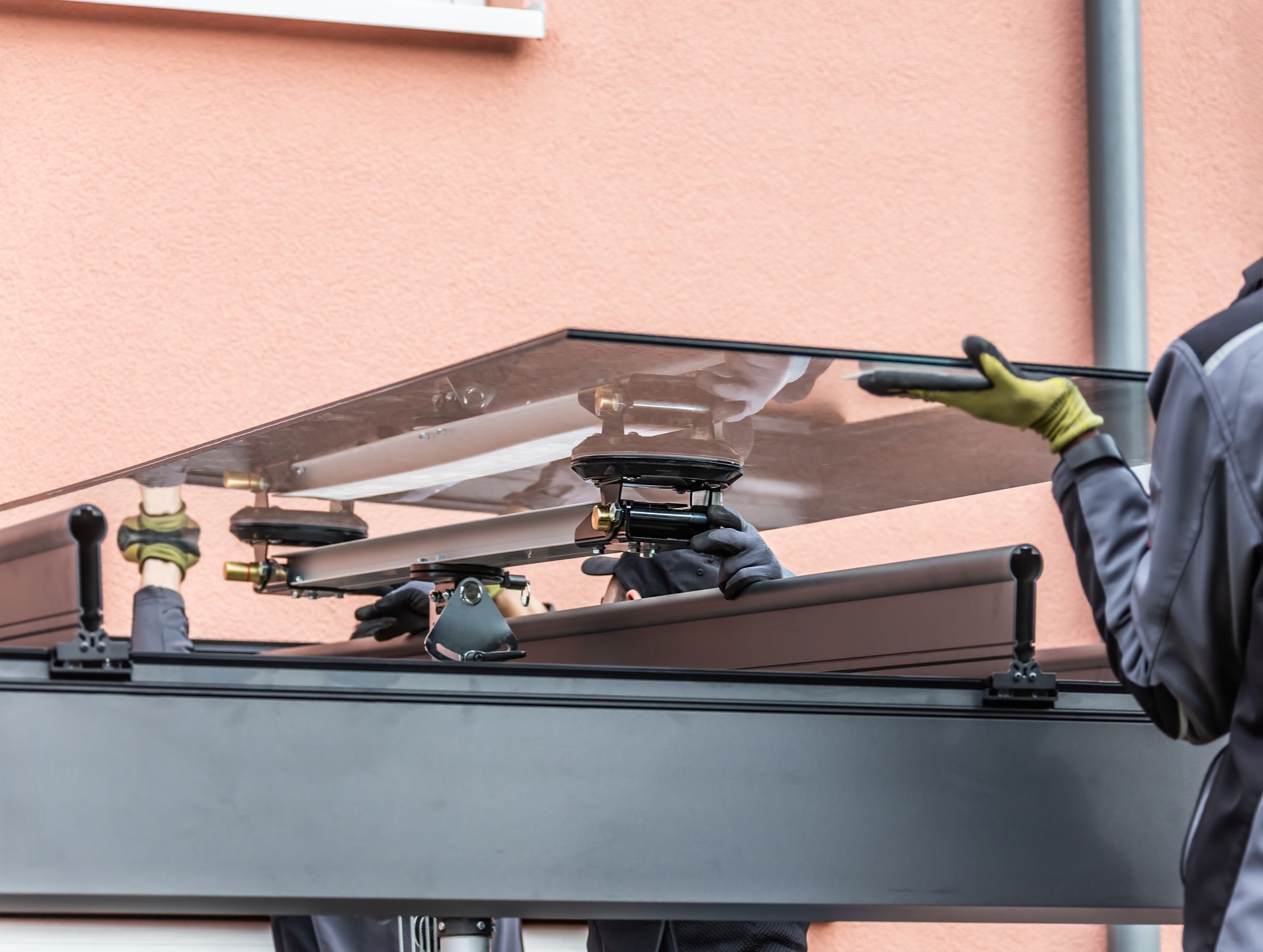 Workers installing a glass canopy using suction tools on a building exterior.