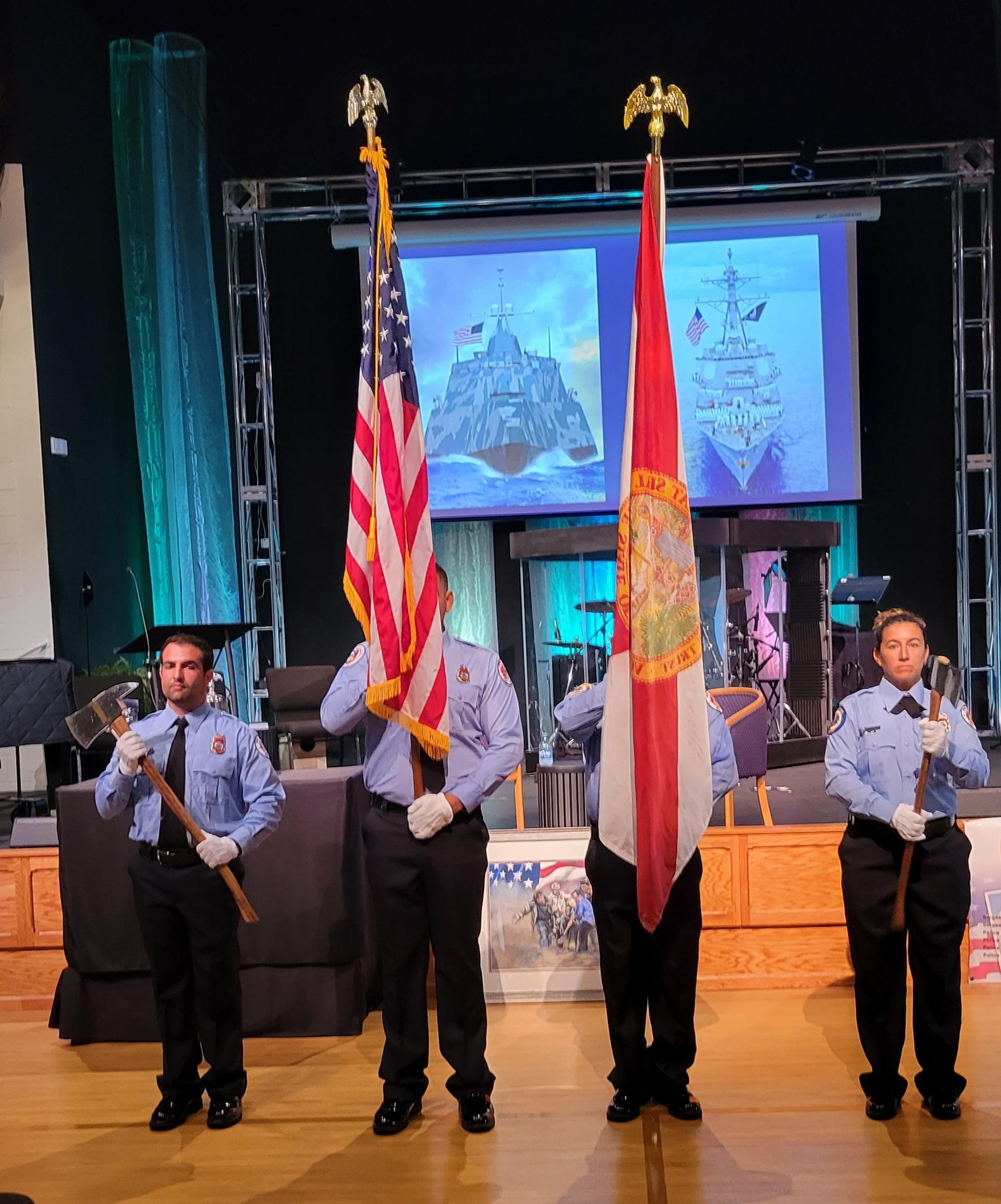 Four uniformed officers stand holding U.S. and Florida flags on a stage with a screen behind them.