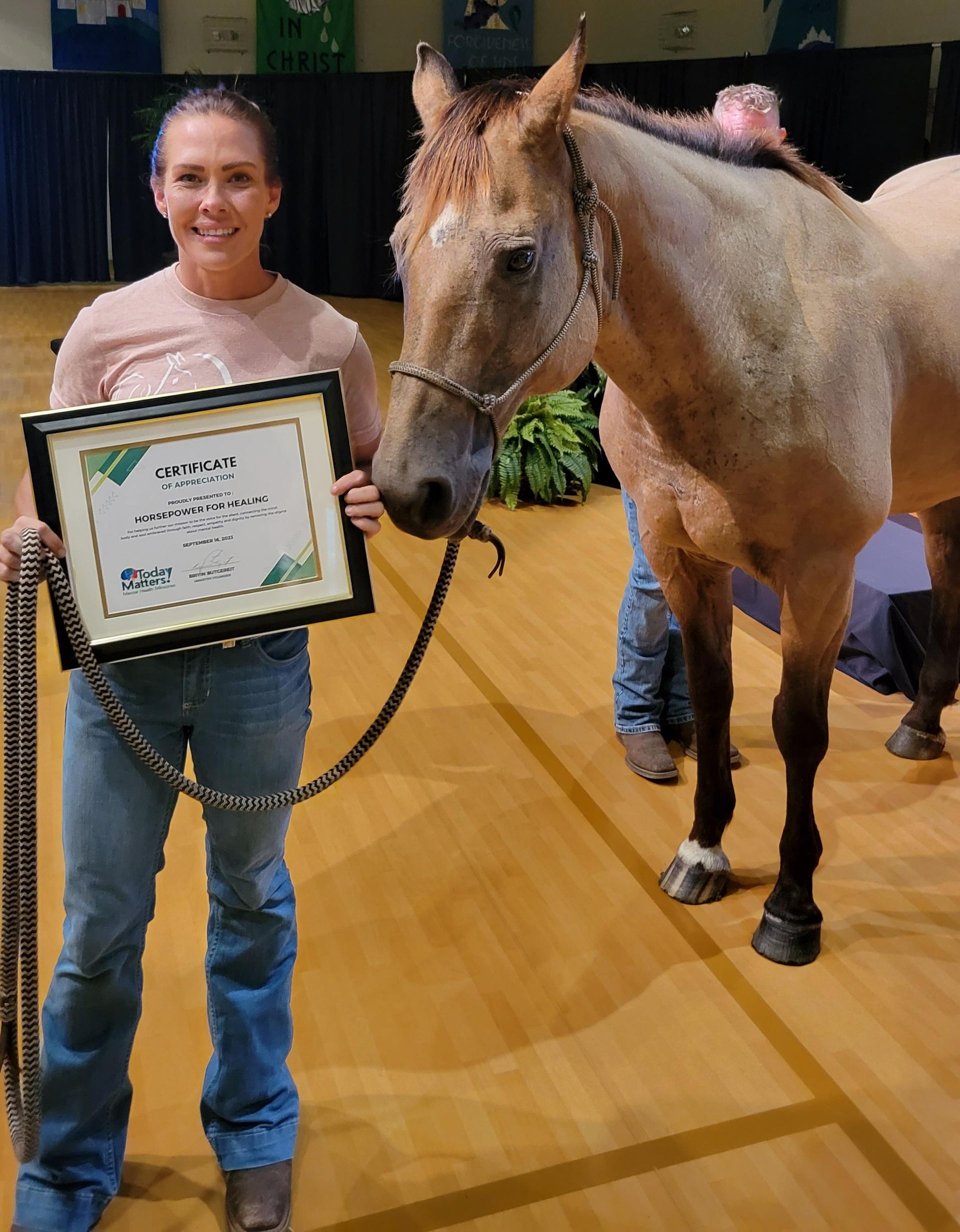 Woman holding framed certificate beside a small horse in an indoor arena
