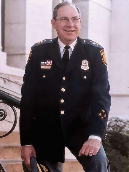 A man in a police uniform is smiling and holding a hat