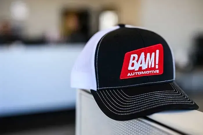 Black and white BAM! Automotive cap on a chair. Red logo on the front.