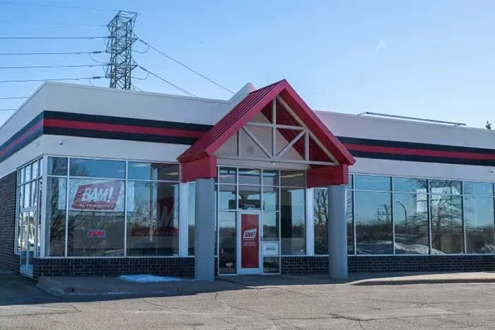 Exterior of a store with a red and white awning and trim, large windows, and a clear sky.