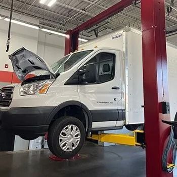 White box truck raised on a lift in a garage with the hood open.