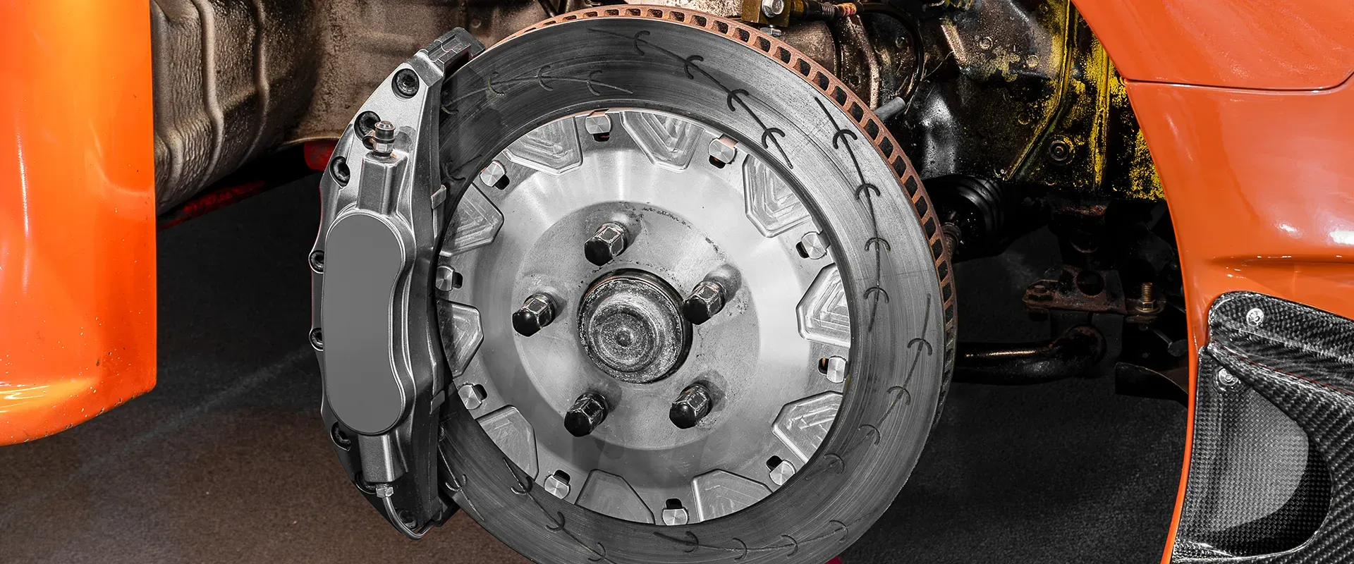 Close-up of a car's brake disc with a gray caliper. Orange car body is on the right and left.