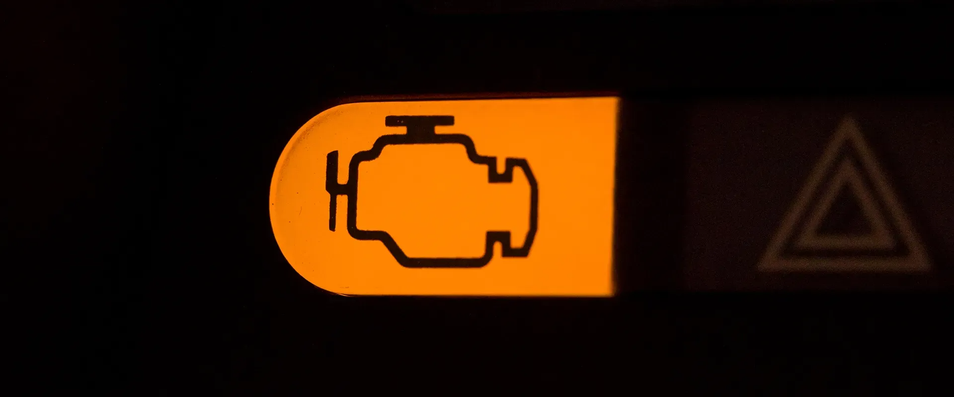 Illuminated engine warning light and hazard light symbol on a car dashboard.
