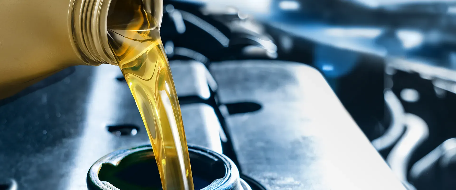 Pouring oil into a car engine. Yellow oil flows from a bottle into the engine's oil fill cap.