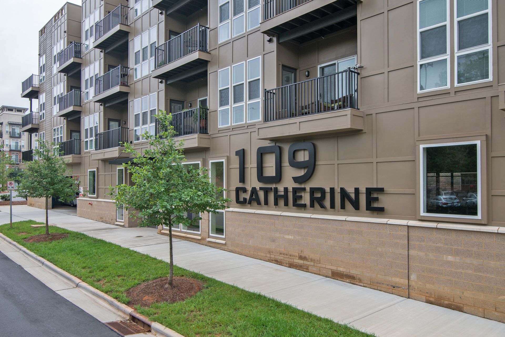 Exterior of 109 Catherine apartments; modern building with balconies, large signage, and trees along the sidewalk.